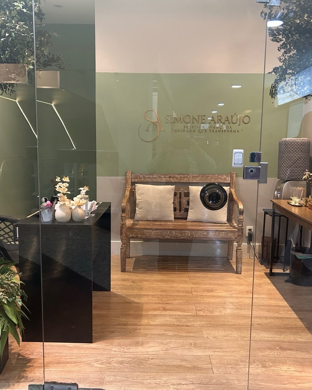Recepção da Simone Araujo Estética, com parede verde, marca dourada e banco de madeira